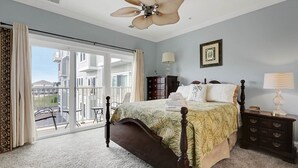 A bedroom with a large bed, a ceiling fan, a dresser, and a nightstand. There is a sliding glass door leading to a balcony. - Do you want to go to the beach "Oar Knot"? (Carolina Beach)