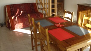 Un comedor con una mesa de madera, sillas y un mantel individual rojo y azul. Se ve una escalera de madera y una estantería con libros al fondo.