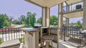 Un patio techado al aire libre con mobiliario de madera, una parrilla y vistas a una carretera y árboles.