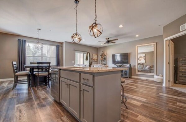A spacious kitchen with a central island, wooden flooring, and pendant lighting.