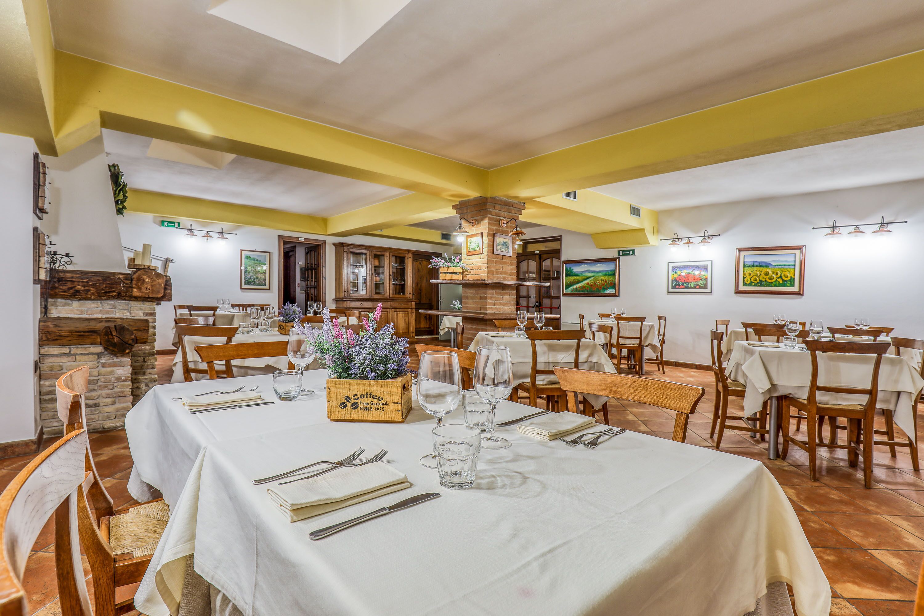A restaurant with white tablecloths, wooden chairs, and a brick fireplace.