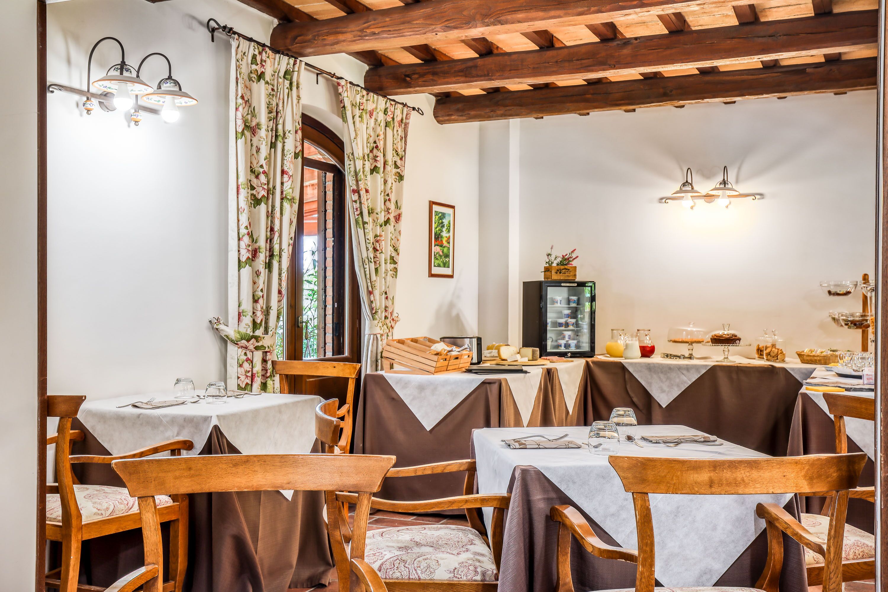 Un espace repas avec des tables et des chaises en bois, des rideaux à motifs floraux et un plafond en bois.