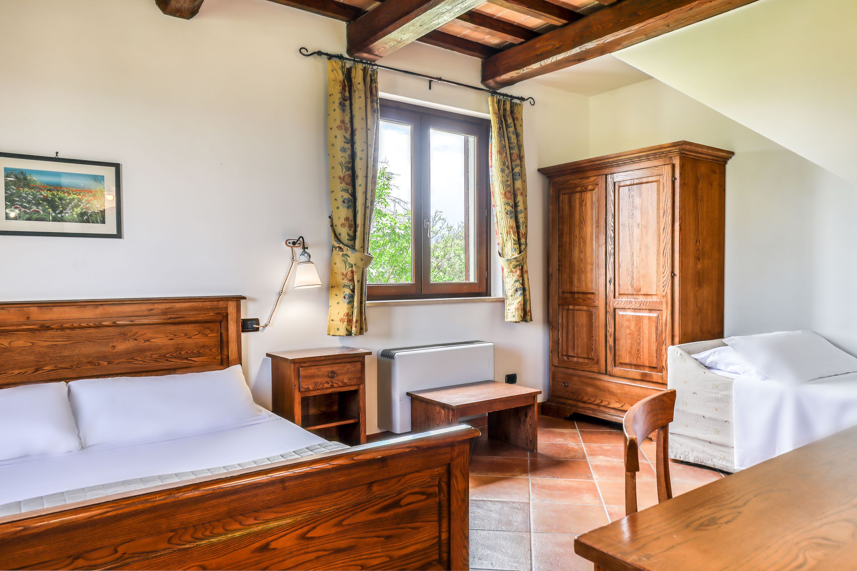 A bedroom with a wooden bed, a desk, a chair, a wardrobe, and a window with curtains.