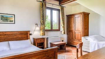 A bedroom with a wooden bed, a desk, a chair, a wardrobe, and a window with curtains.