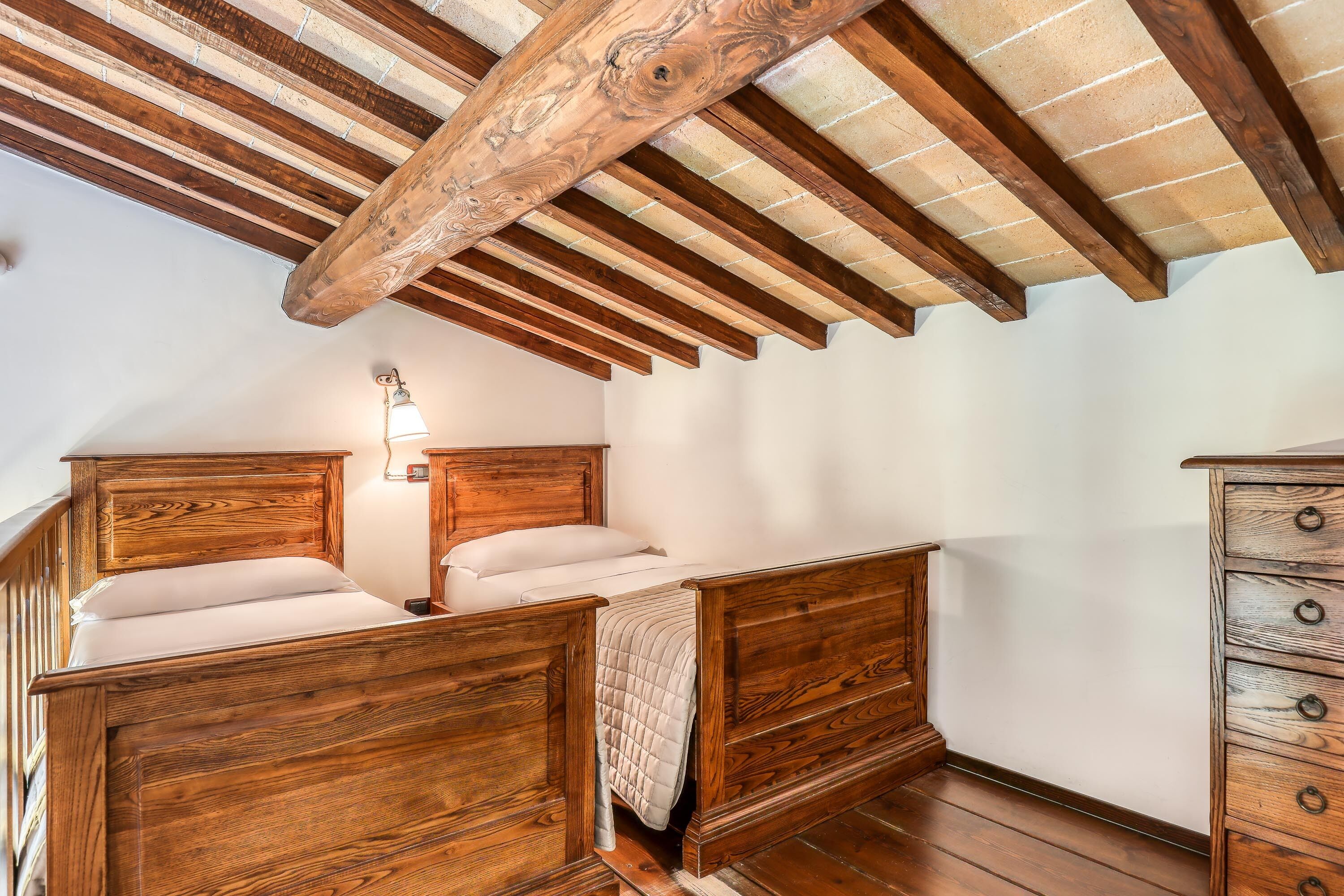 A bedroom with wooden furniture, a sloped ceiling, and a wall-mounted light fixture.