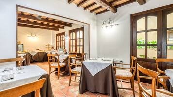 A dining area with wooden tables and chairs, a tiled floor, and a wooden ceiling.