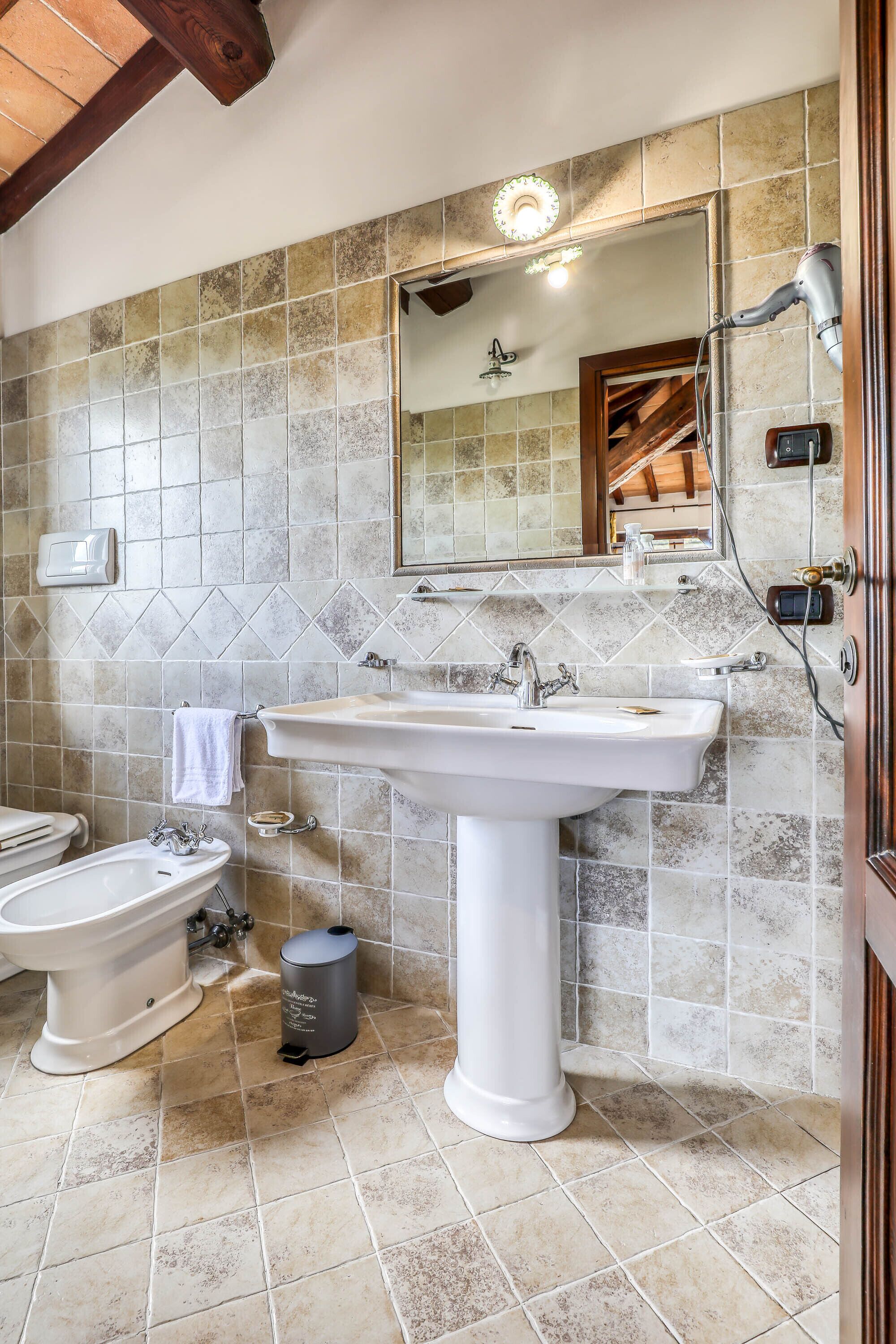 Un baño con lavamanos pedestal, un bidé, un espejo y un cabezal de ducha.