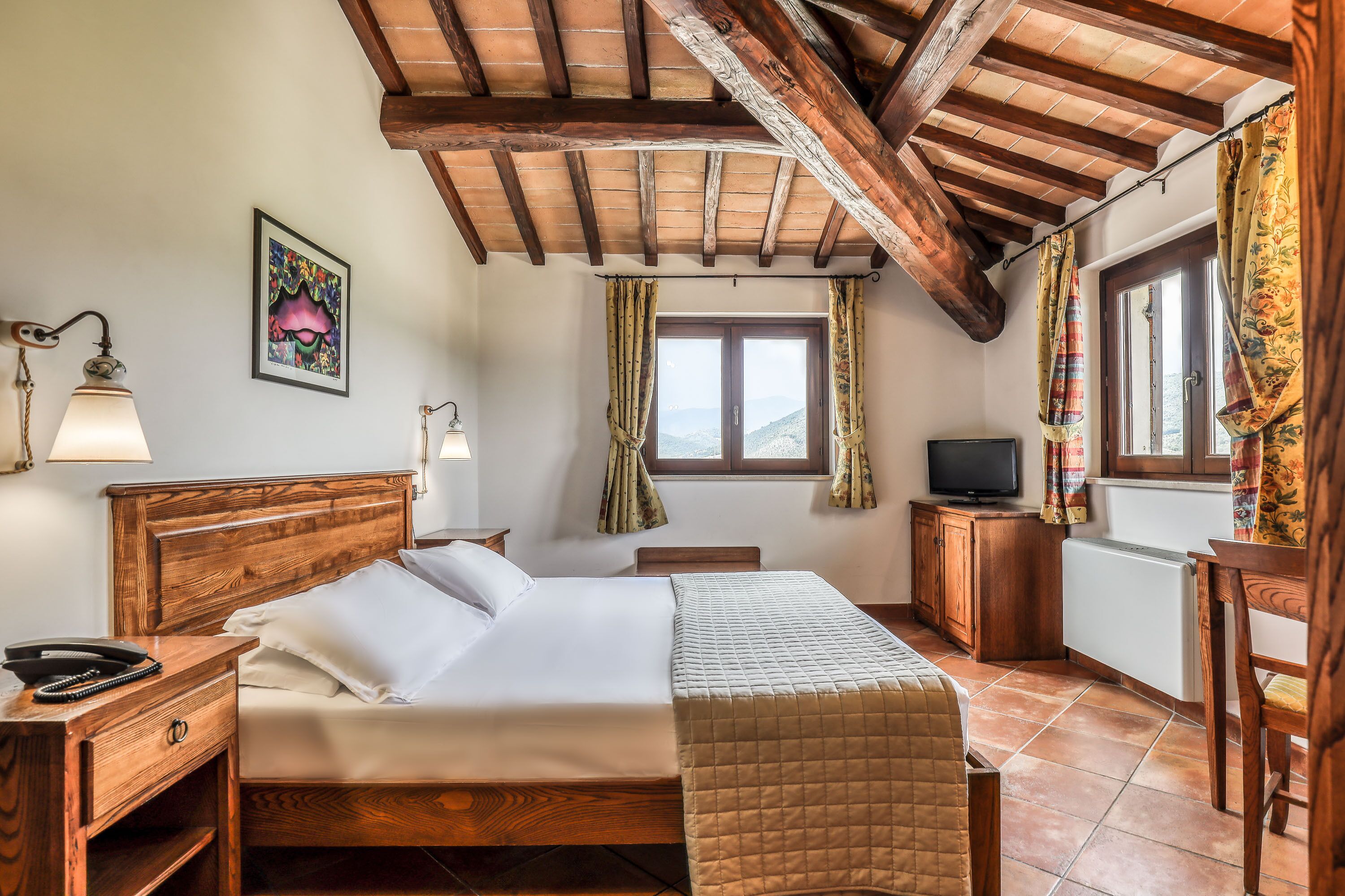 A bedroom with a wooden bed, a television, and a window with curtains.