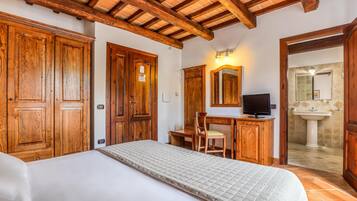 A bedroom with a bed, wooden wardrobe, desk with chair, and a TV.