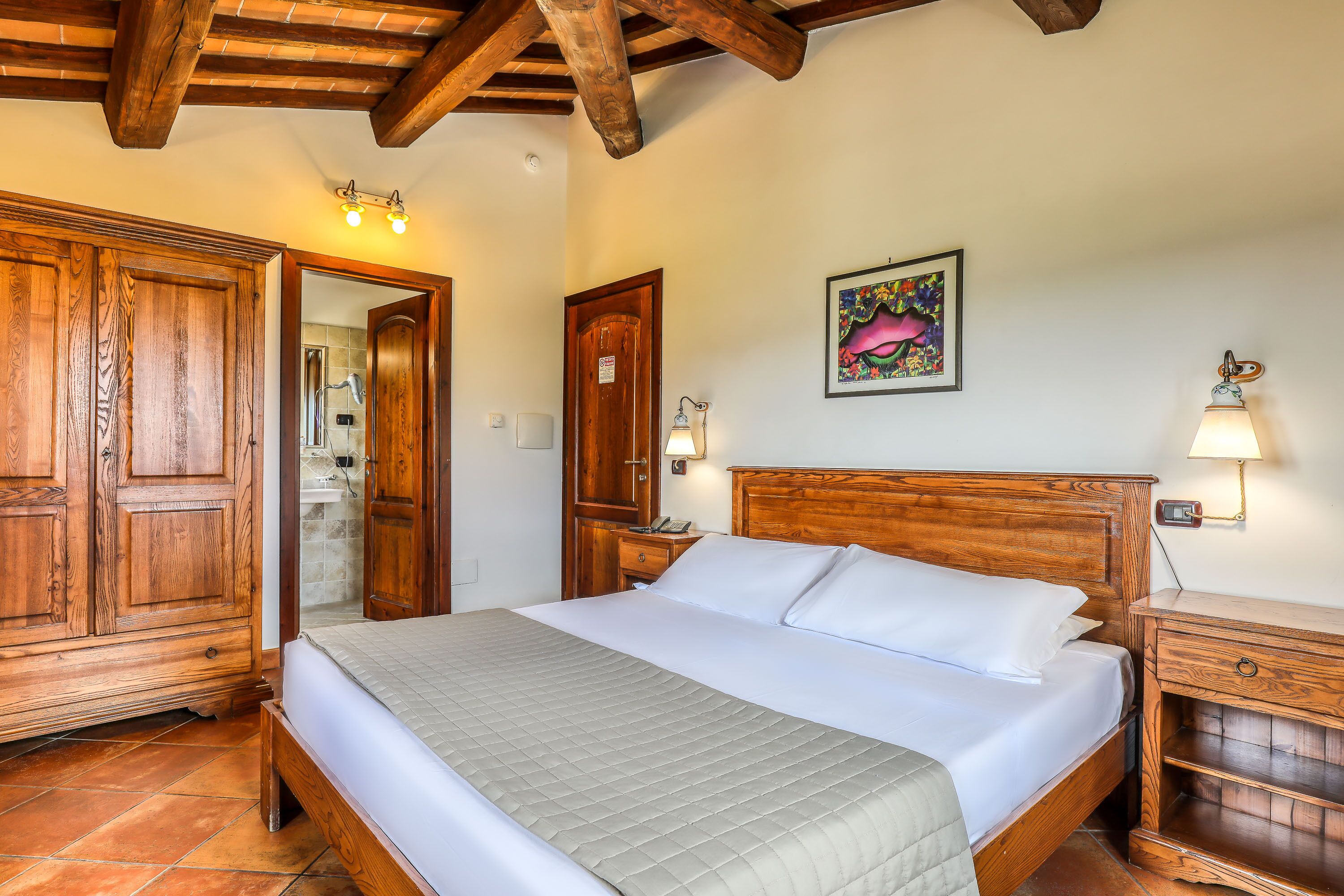 A bedroom with a wooden bed, a wooden wardrobe, a nightstand with a lamp, and a painting on the wall.