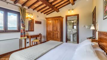 Ein Schlafzimmer mit Bett, Holzschrank, Schreibtisch, Stuhl und Blick ins Bad.