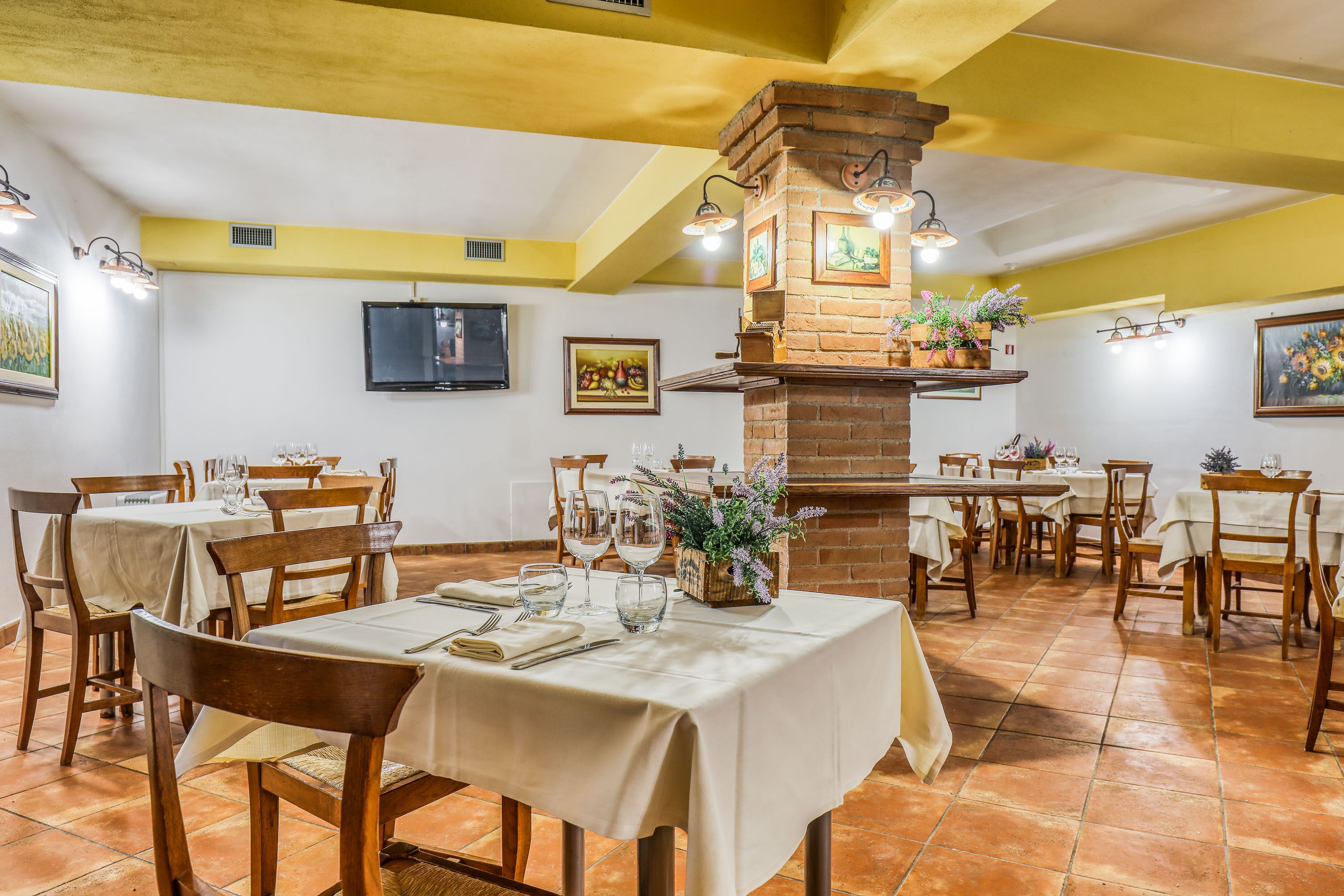 A restaurant with multiple tables set for dining, a brick fireplace, and wall-mounted artwork.