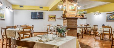 Un restaurante con varias mesas dispuestas para comer, una chimenea de ladrillo y obras de arte colgadas en la pared.