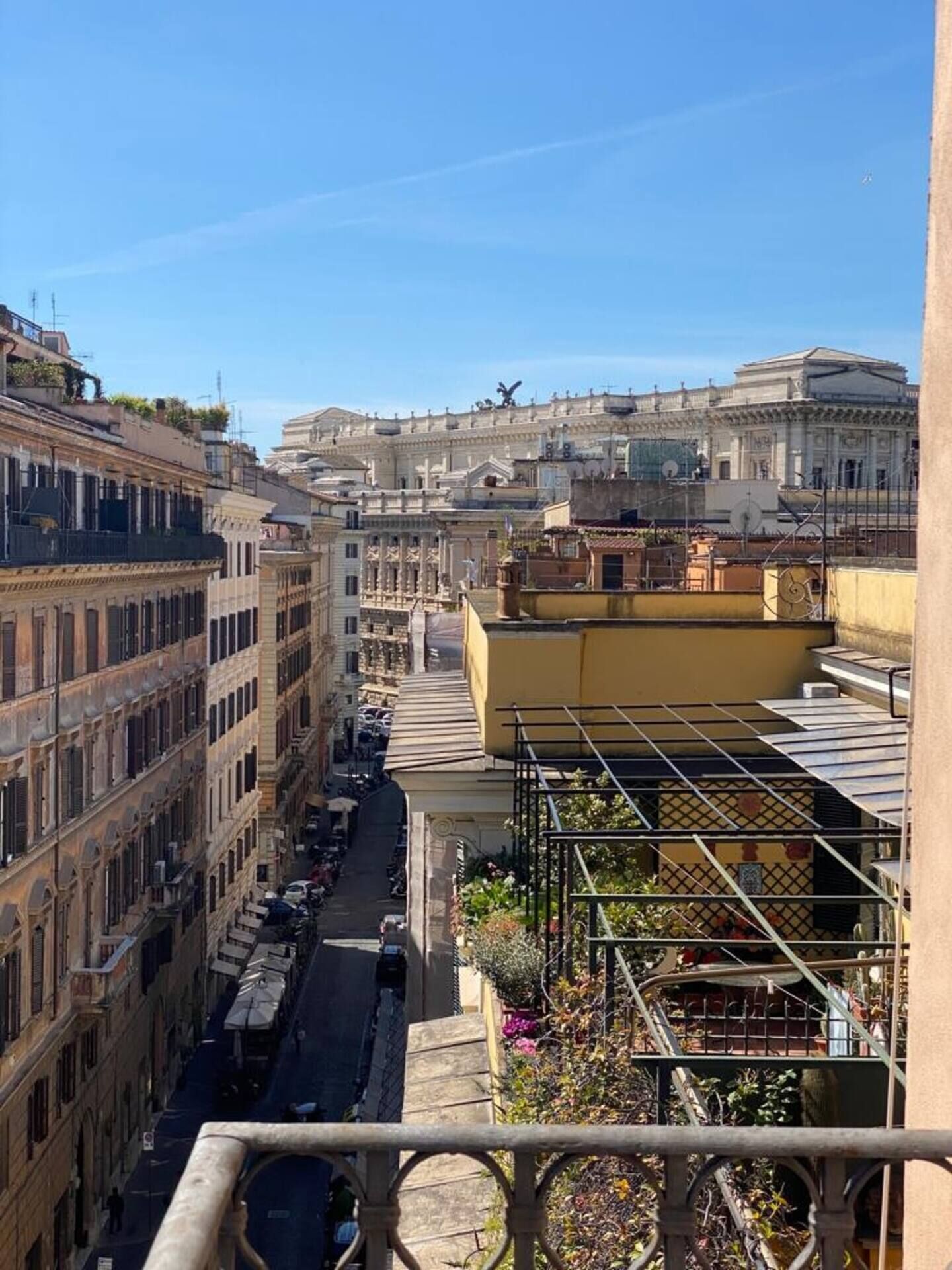 A narrow street with buildings on both sides, a clear sky, and a view of a large classical building in the distance.