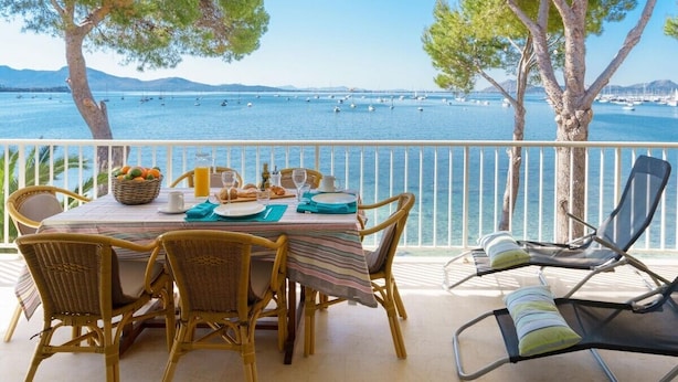 A dining area with a table set for four, overlooking a body of water with boats. - Pine Walk Xisco apartment by Vida Villas (Pollença)