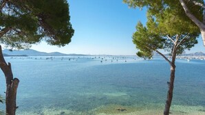 A coastal view with clear water, boats, and a distant bridge. - Pine Walk Xisco apartment by Vida Villas (Pollença)