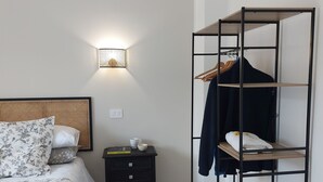 Une chambre à coucher comprenant un lit, une table de chevet, une étagère fixée au mur avec des vêtements et une lampe murale.