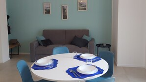 Un coin repas avec une table ronde dressée pour quatre personnes, des chaises bleues et un luminaire suspendu.