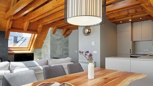 A modern kitchen with wooden beams, a dining area with a wooden table, and a living space with a sofa and a skylight. - Les Marmottes by FeelFree Rentals (Vielha)