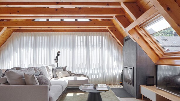 A modern loft bedroom with a sloped ceiling, a large window with sheer curtains, a built-in TV, and a cozy seating area with a sofa and coffee table. - Les Marmottes by FeelFree Rentals (Vielha)