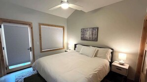 A bedroom with a bed, a nightstand, a ceiling fan, a window with blinds, and a door. - Elk Valley- Views for days (Crested Butte)
