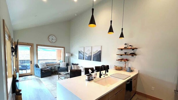 A modern kitchen with a large island, pendant lighting, and a view to a living area. - Elk Valley- Views for days (Crested Butte)