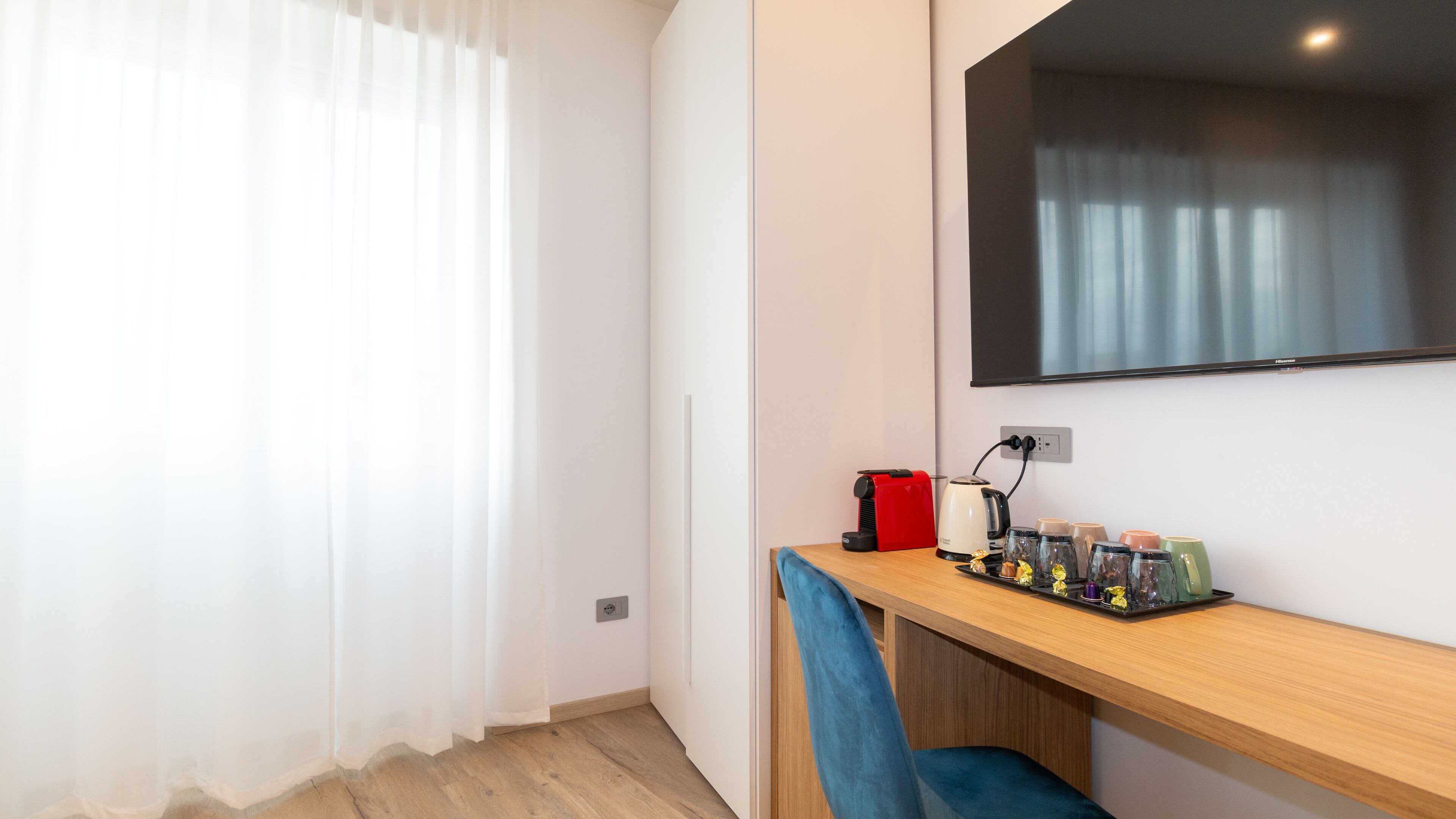 Een moderne kamer met een houten bureau, een flatscreen-tv aan de muur, een rode toaster, een waterkoker, en een dienblad met snacks.
