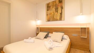 A hotel room with a neatly made bed, a headboard with built-in lighting, a painting on the wall, and a bedside table with a lamp.