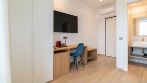 A modern hotel room with a wooden desk, a blue chair, a flat-screen TV mounted on the wall, and a white sink with a mirror. - Galleria Roma Art Guesthouse (Oristano)