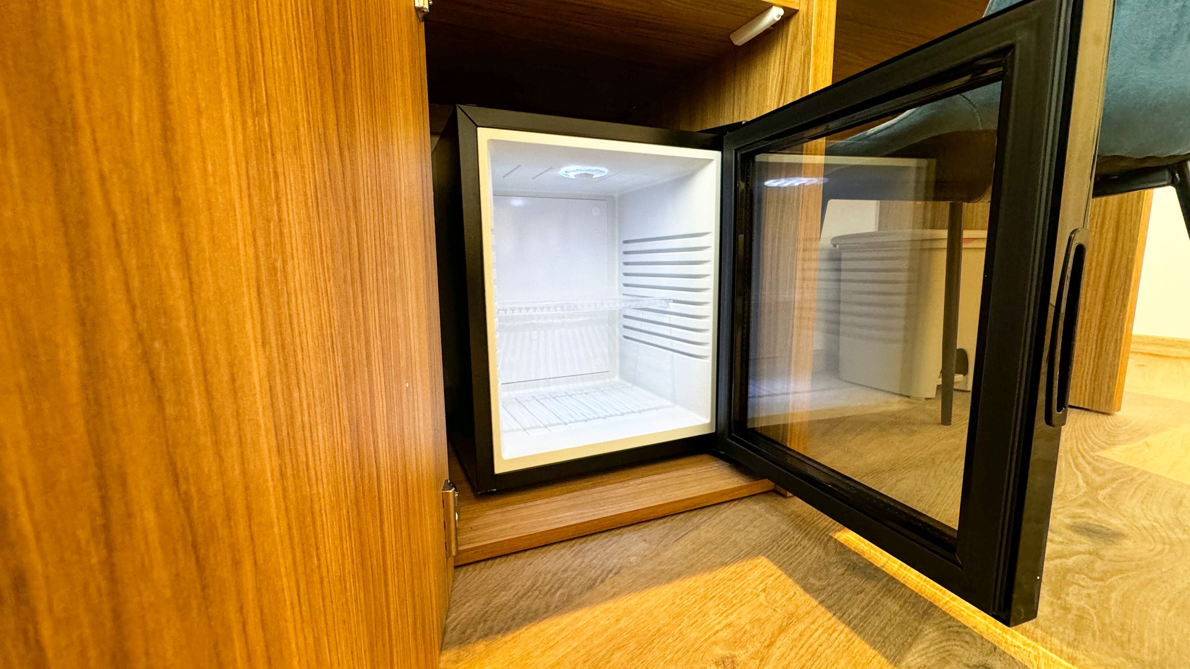 A compact, modern room with a built-in refrigerator and a wooden floor.