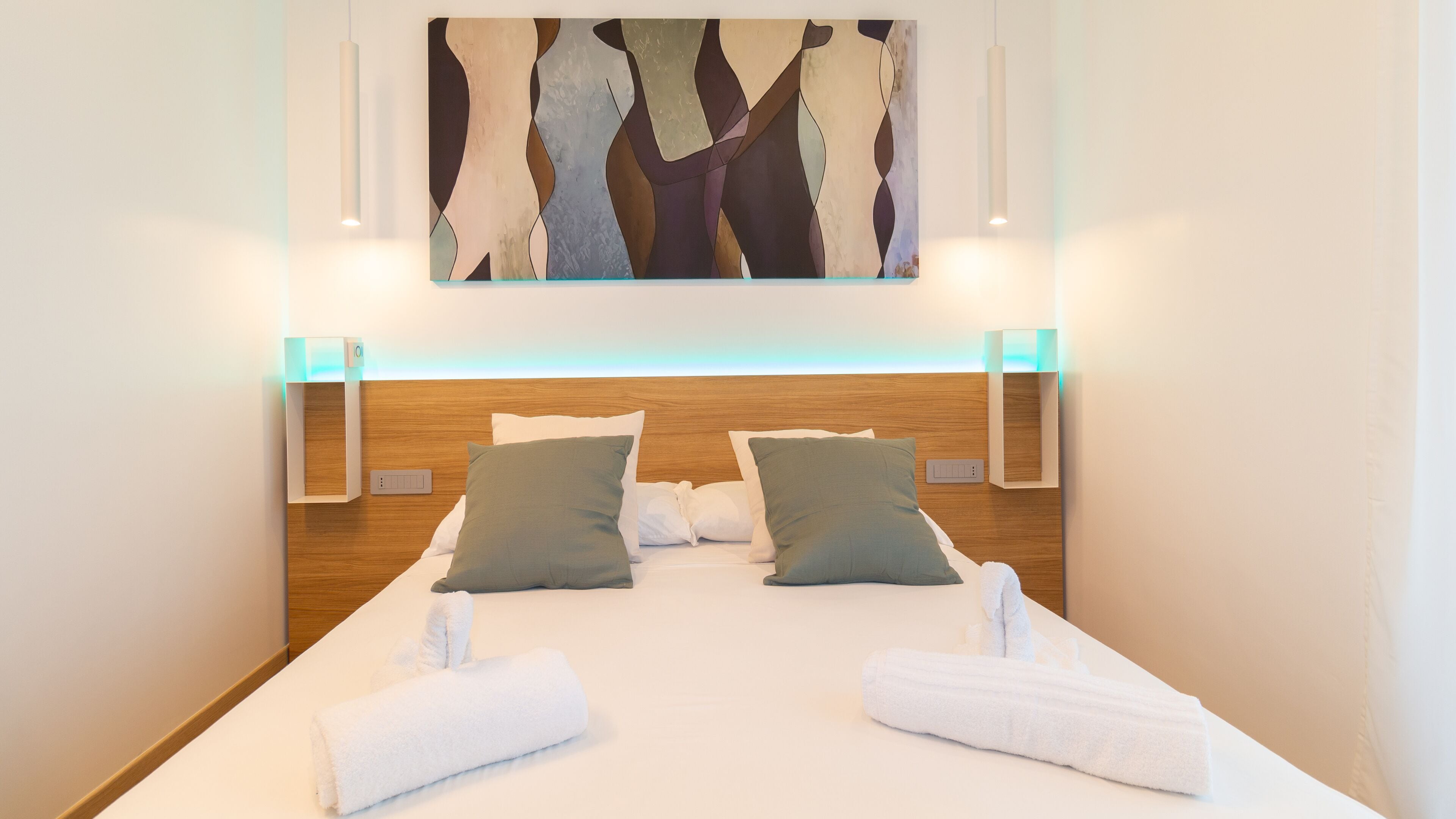 A hotel room with a wooden headboard, two pillows, a neatly made bed, and a painting above the bed.