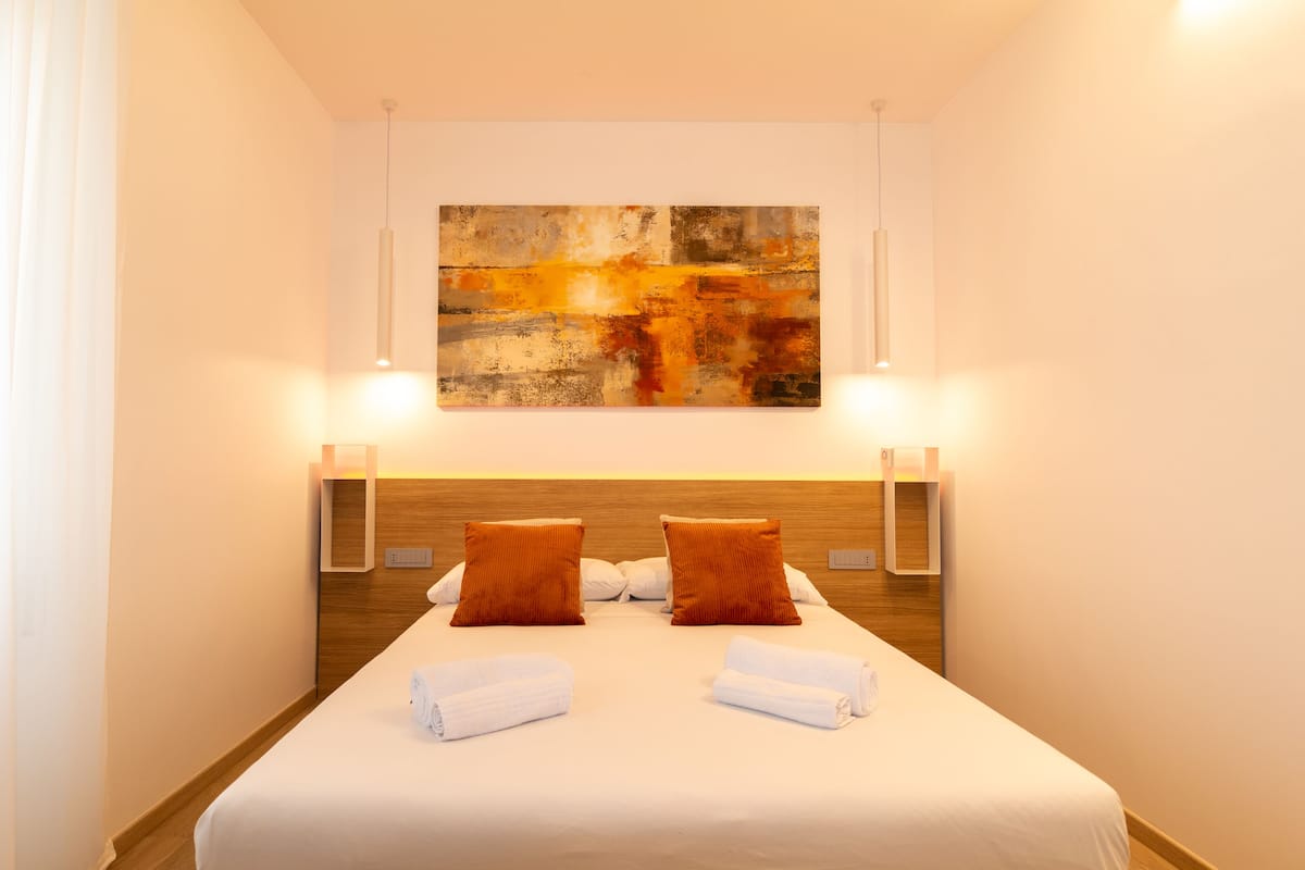A hotel room with a large bed, two pillows, a headboard, bedside lamps, and a painting on the wall.
