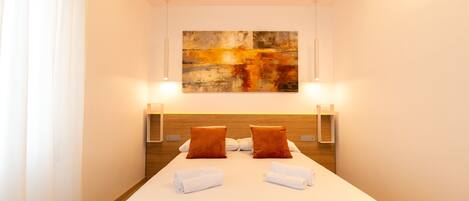 Habitación de hotel con una cama grande, dos almohadas, cabecero, lámparas de noche y un cuadro en la pared.