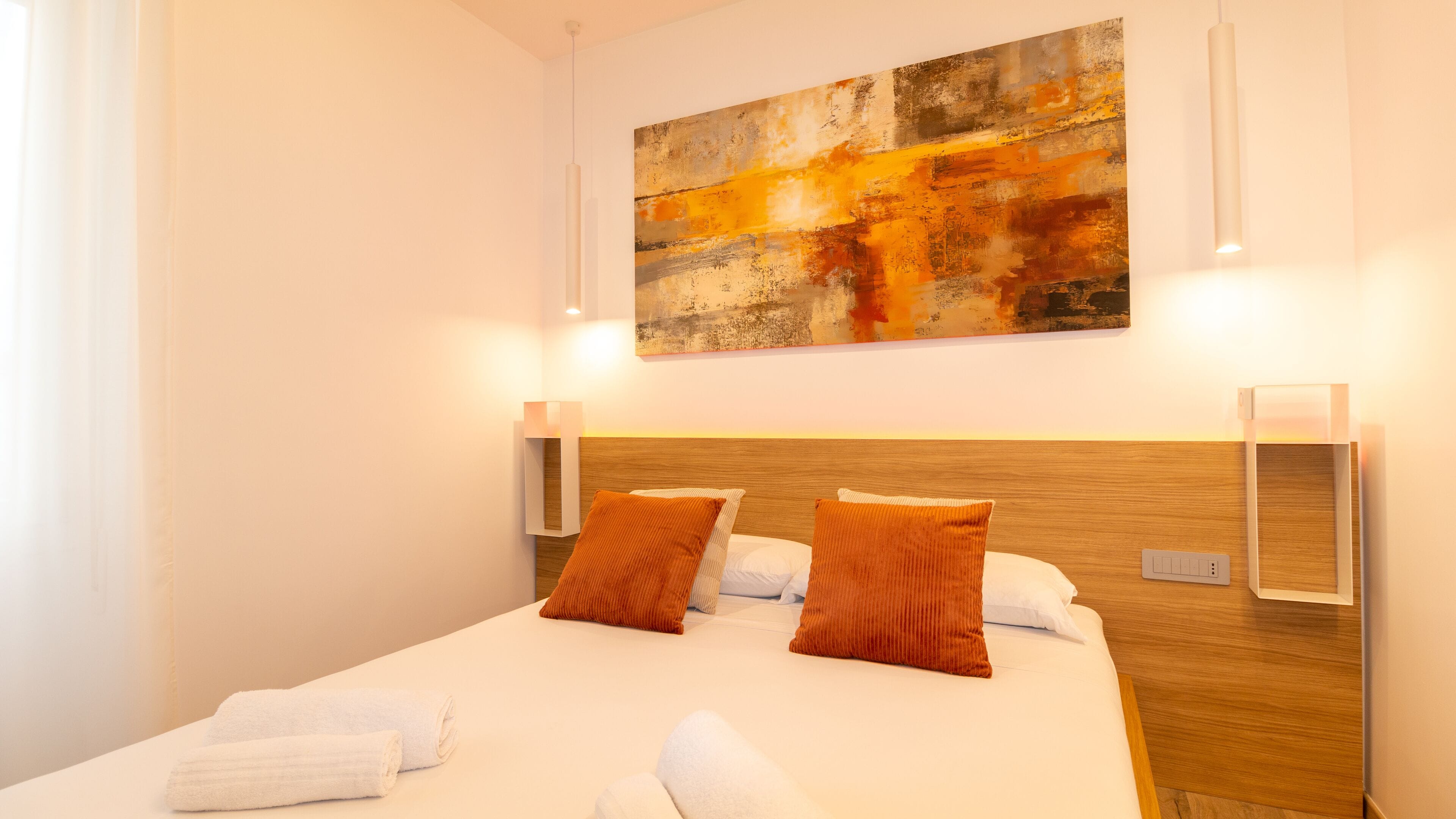 A hotel room with a large bed, two wall-mounted lamps, and a large abstract painting on the wall.