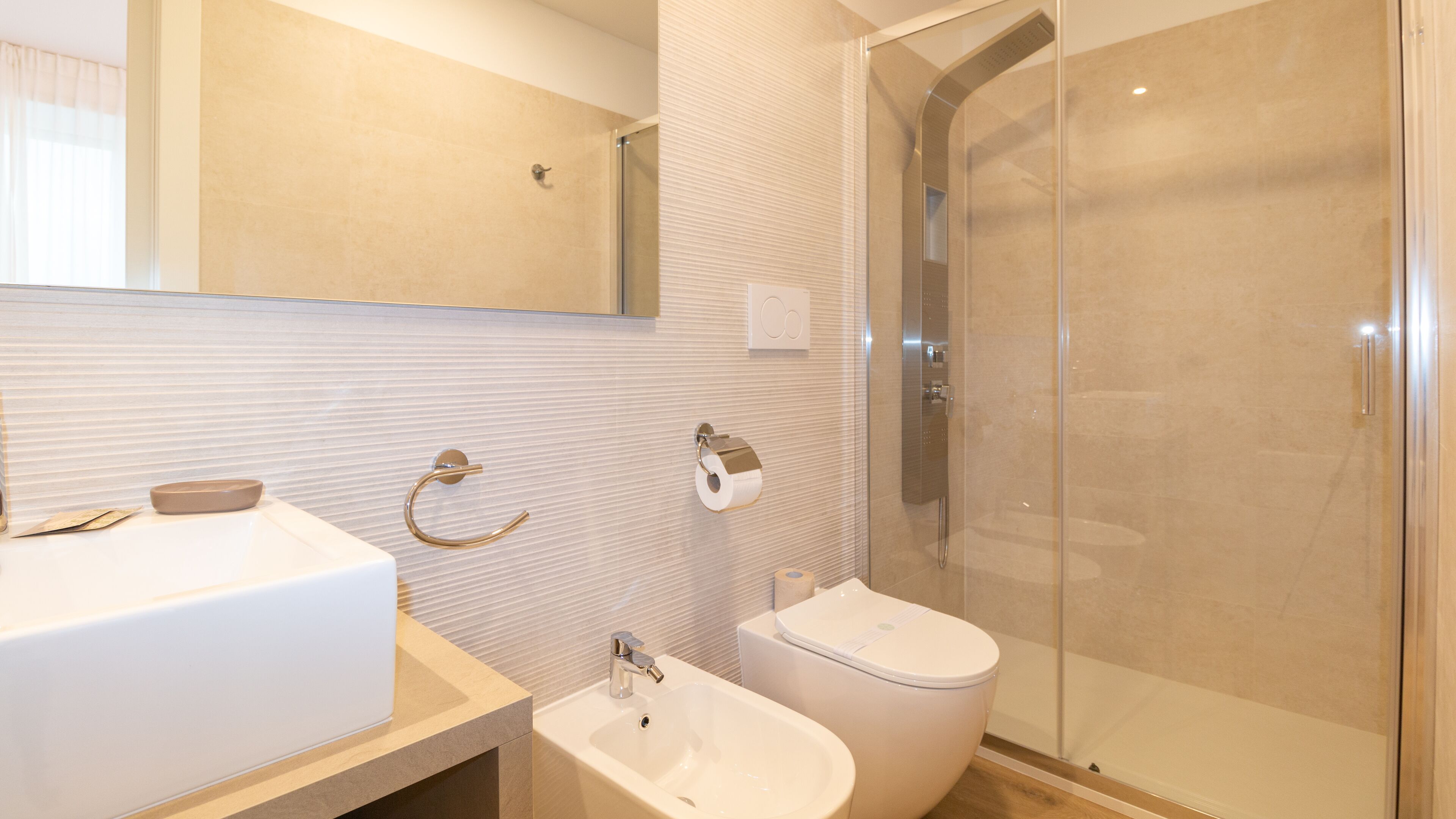 A modern bathroom with a large mirror, a sink, a bidet, and a glass-enclosed shower.