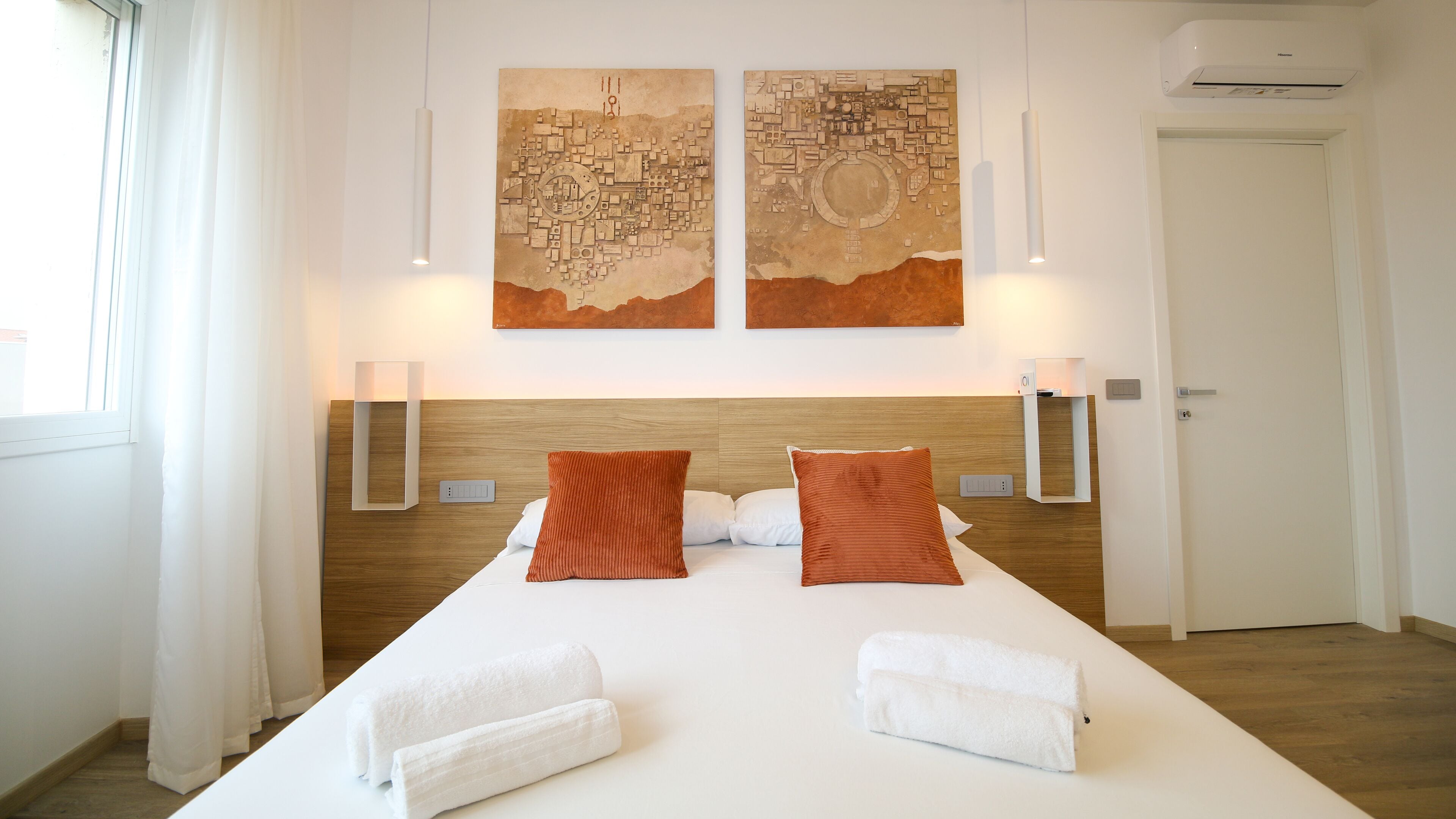 Una habitación de hotel con una cama grande, dos lámparas de pared y dos cuadros abstractos sobre la cama.