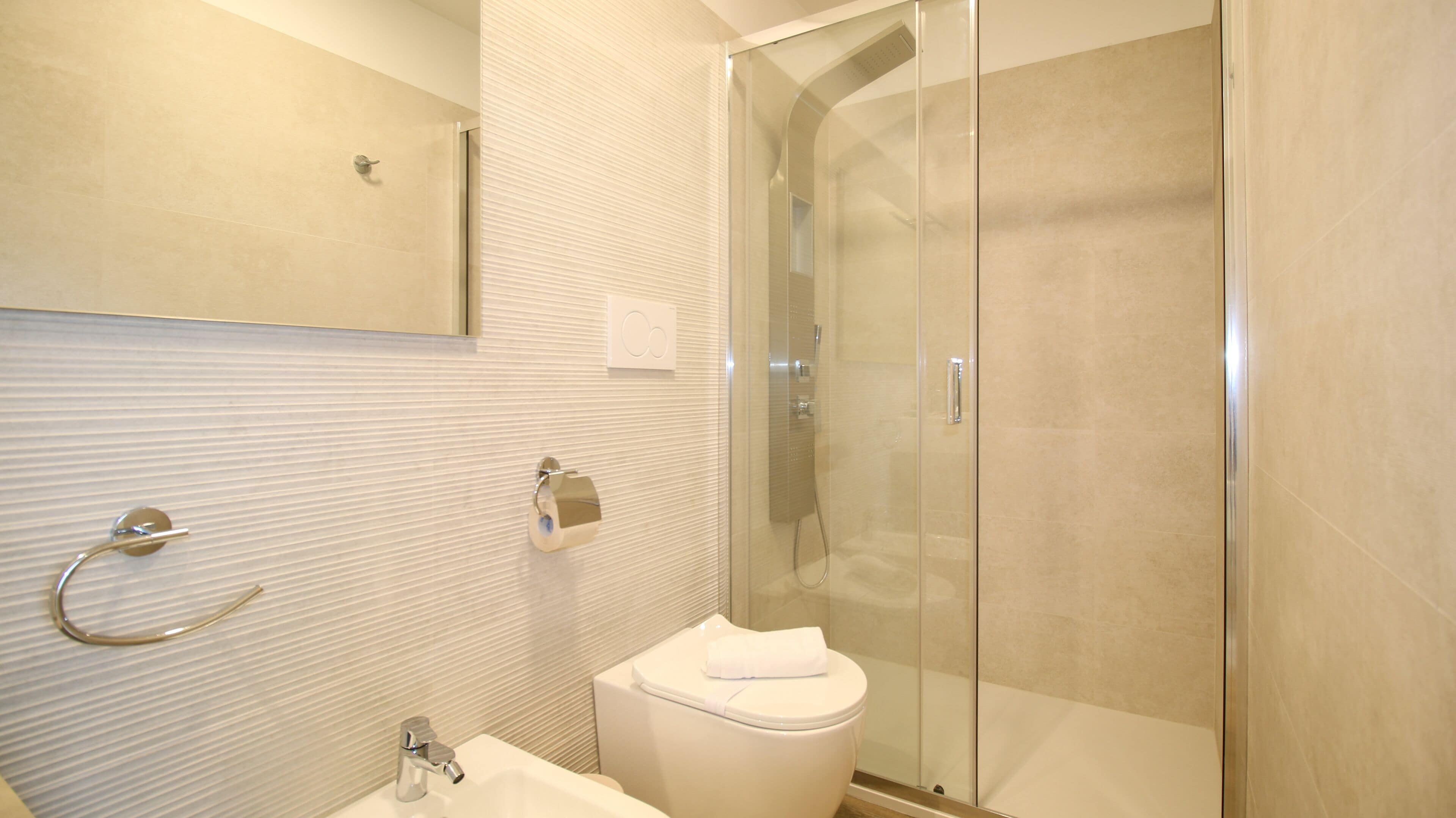 Une salle de bain moderne avec une douche à parois de verre, des toilettes et un lavabo sur lequel est posée une serviette.