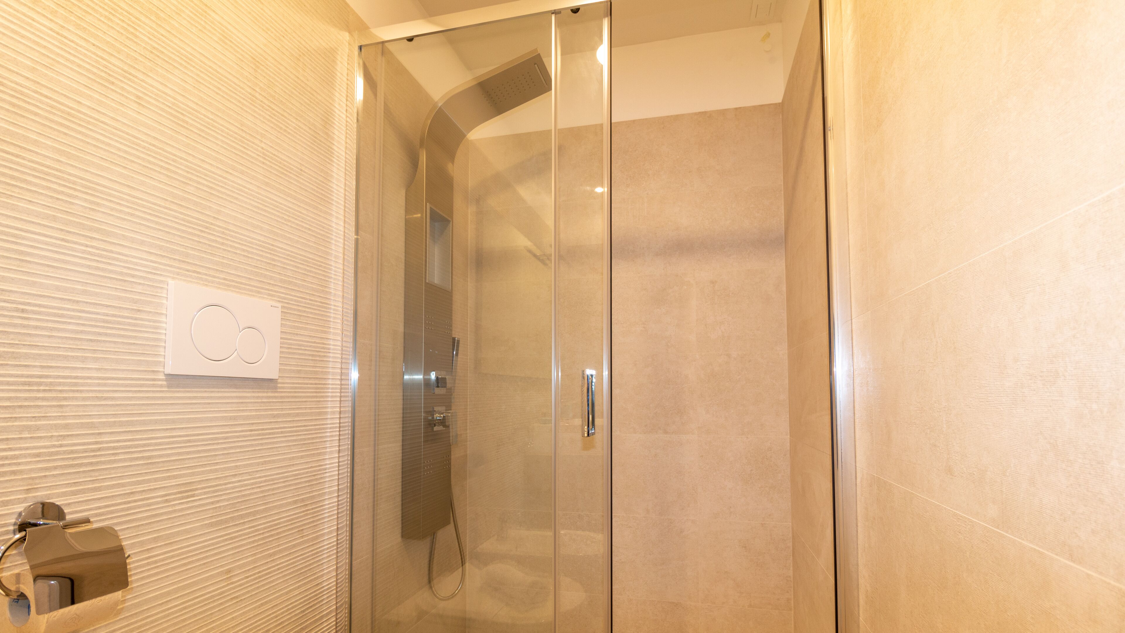 A modern bathroom with a glass-enclosed shower, a towel rack, and a wall-mounted light switch.