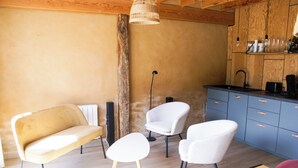 A modern kitchen with wooden cabinets, a dining area with a sofa and chairs, and a hanging light fixture. - Oude Schuur Omgetoverd tot Moderne Gîte (montchevrier)