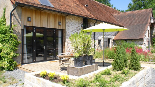 A stone building with a wooden deck, a large umbrella, and potted plants. - Oude Schuur Omgetoverd tot Moderne Gîte (montchevrier)
