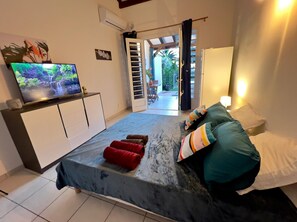 Une chambre à coucher avec un lit, un téléviseur posé sur un meuble, une porte donnant sur l’extérieur et une table de chevet avec une lampe.