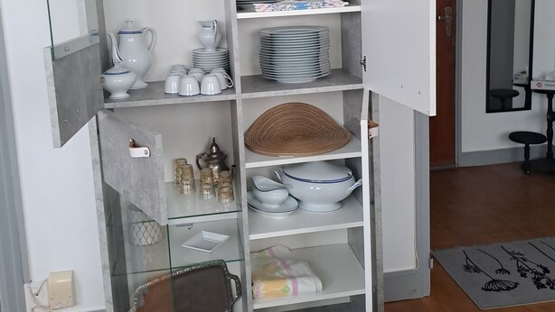 Una cocina con estantes abiertos que contienen varios platos, vasos y un posavasos tejido.