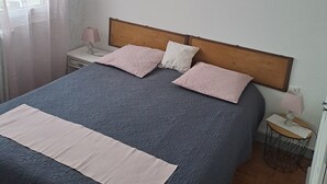 Un dormitorio con cama, mesitas de noche, una lámpara, un cuadro en la pared y una ventana con cortinas.