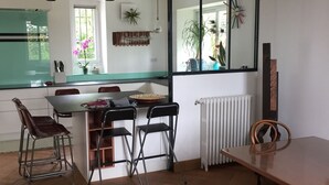 Une cuisine moderne avec un coin repas, dotée d’une grande fenêtre, de luminaires suspendus et d’un radiateur.