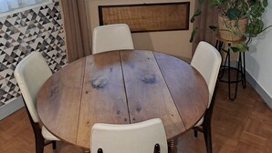 Ein runder Holztisch mit vier Stühlen, einem Topfpflanzen und einem Fenster mit transparenten Vorhängen.