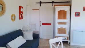 Un salon avec un canapé bleu foncé, une table blanche et une chaise blanche. On y trouve une porte blanche avec une bande rouge et un meuble en bois dont la base est blanche.