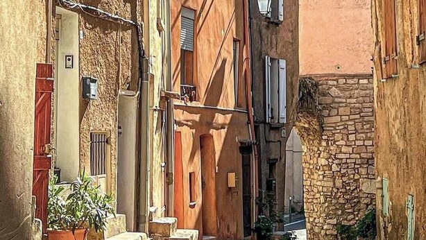 Une rue étroite bordée de bâtiments traditionnels, un mur de pierre et un pot de fleurs.