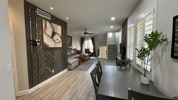 Une cuisine moderne avec un parquet en bois disposé en chevrons, un coin repas avec une table et des chaises en bois foncé, et un salon avec un canapé et une grande œuvre d’art murale.
