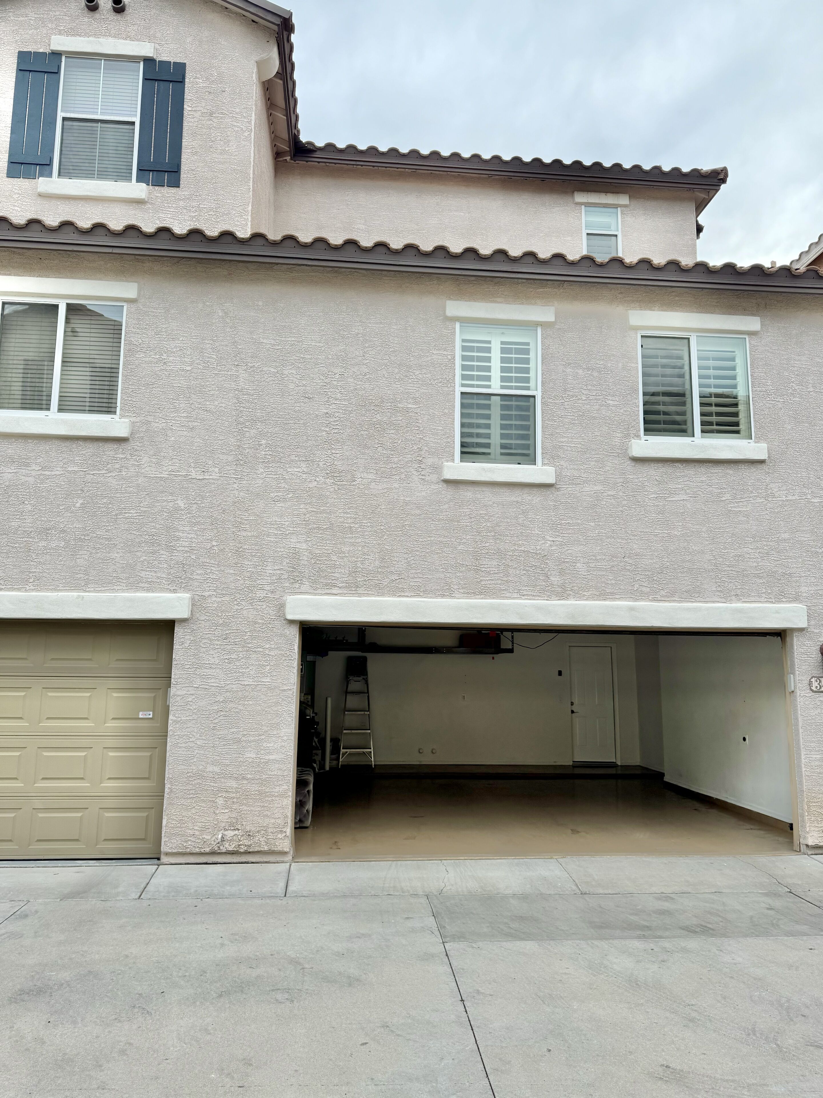 A two-story house with a garage, two windows with shutters, and a concrete driveway.