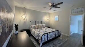 Une chambre à coucher comprenant un lit, un ventilateur de plafond, deux lampes fixées au mur, une fenêtre et une porte.